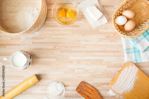 Cutting board, eggs, salt, flour, raw eggs, milk, rolling pin, butter, towel, sieve on light wooden background  with copyspace.