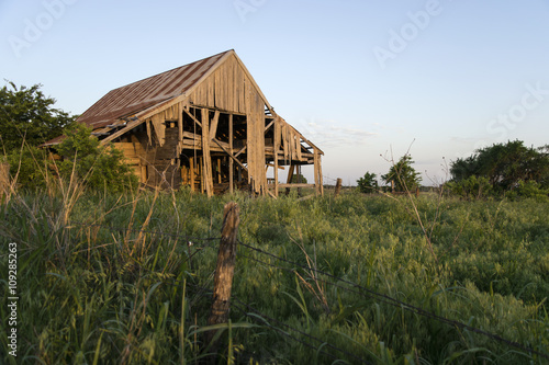 Decaying barn behind fence in field at sunset