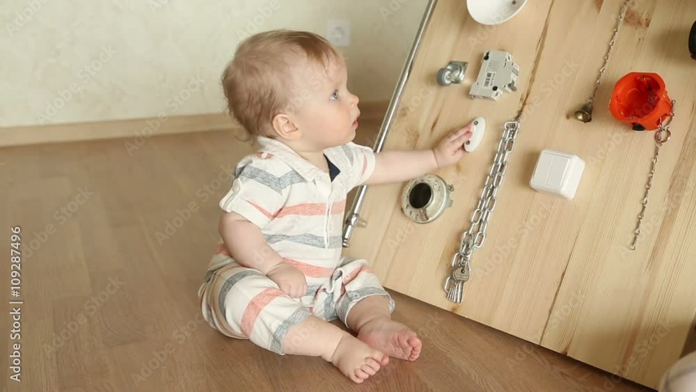 The little boy intently playing with busy board, sitting at the floor The little boy intently playing with busy board, sitting at the floor