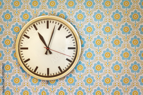 Vintage clock on a wall with retro wallpaper