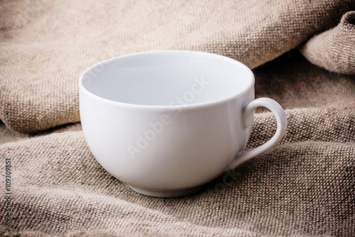 Empty white coffee cup on linen fabric.

