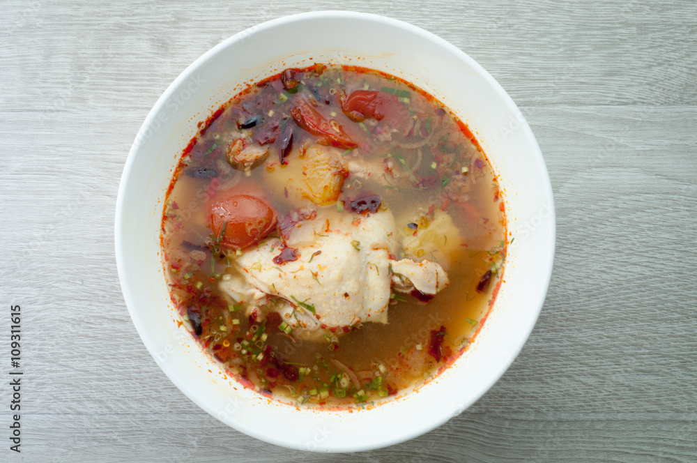 Chicken soup in a white bowl on a wooden floor.