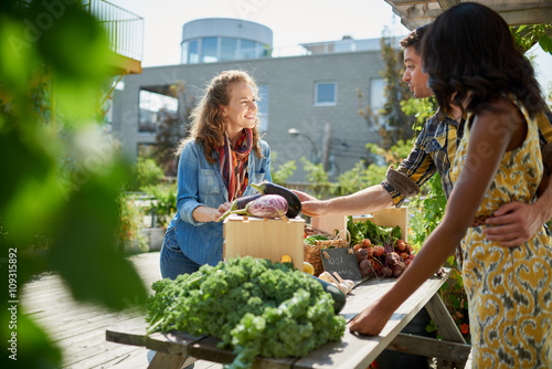 Friendly woman tending an organic vegetable stall at a farmer's market and selling fresh vegetables from the rooftop garden