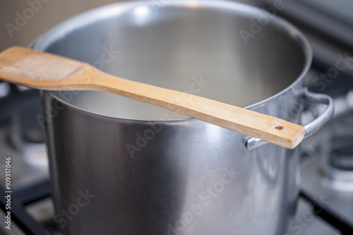Tableau sur toile Wooden spoon over a hot metal pot while cooking a meal on a gas stove