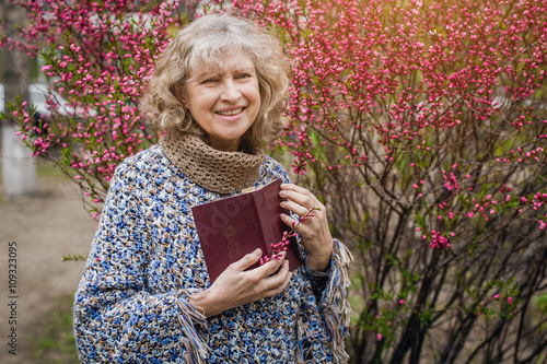 Bilde på lerret an elderly woman with a book in his hands near blooming Apple tree