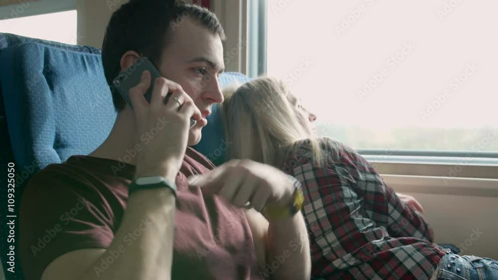 Young angry man talk to somebody on a phone on a moving train. Woman laugh at him Young angry man talk to somebody on a phone on a moving train. Woman laugh at him