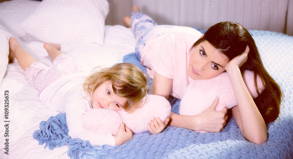 Romantic atmosphere mother and daughter hugging pink soft hearts in bed Romantic atmosphere mother and daughter hugging pink soft hearts in bed