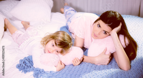 Romantic atmosphere mother and daughter hugging pink soft hearts in bed