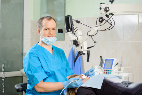 Male dentist working with microscope at modern dentist clinic. Teeth care and tooth health. Dentist checking patient teeth. Oral procedure concept. Stomatology equipment