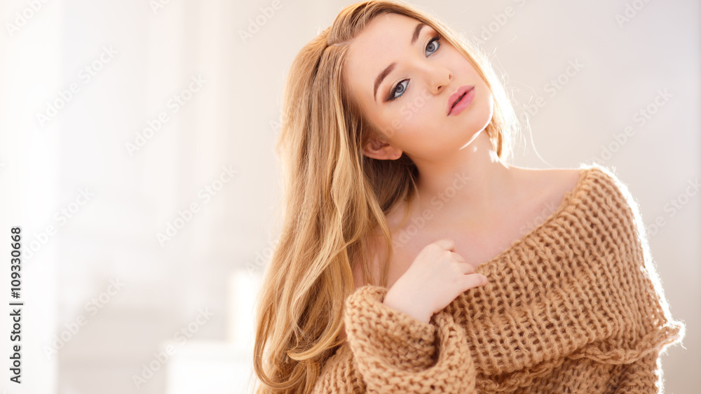 Plakat Young blonde woman in a warm pullover in a light bedroom in a morning