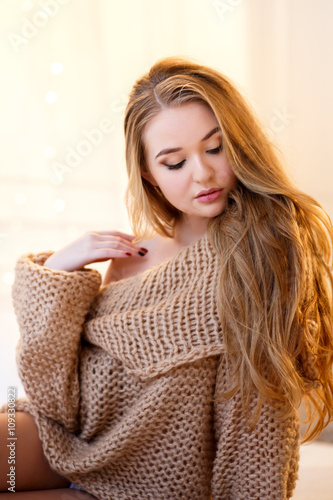 Young blonde woman in a warm pullover in a light bedroom in a morning