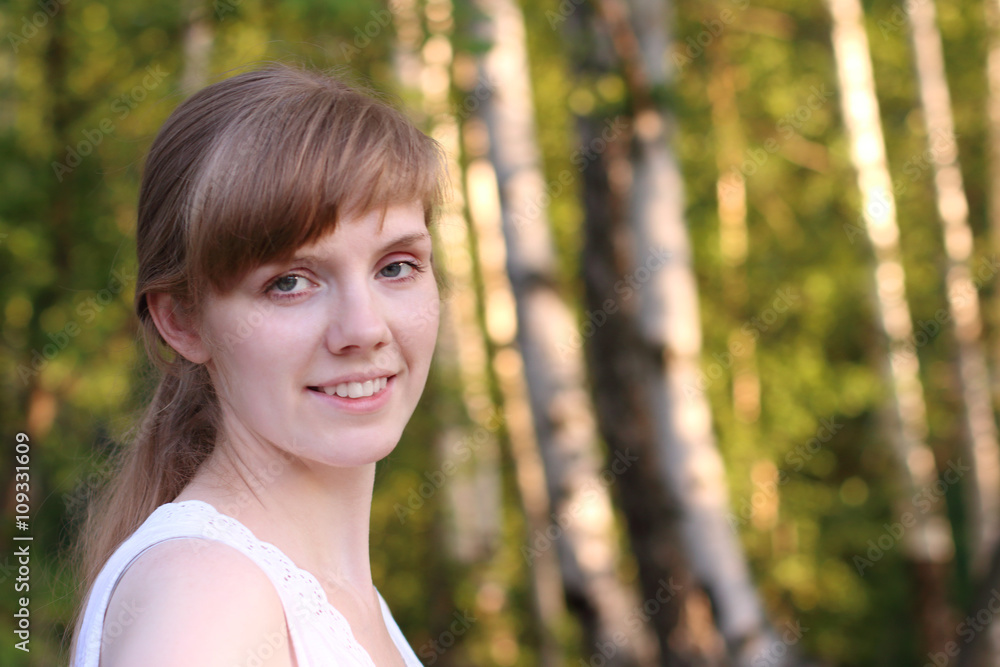 Beautiful young woman in white smiles in sunny summer park Beautiful young woman in white smiles in sunny summer park