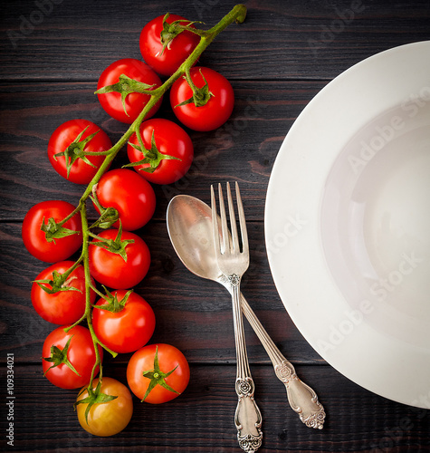 Plate on a wooden table with bunch tomatoes. 