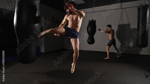 Aggression. muscular handsome fighter giving a forceful forward kick during a practise round with a boxing bag.