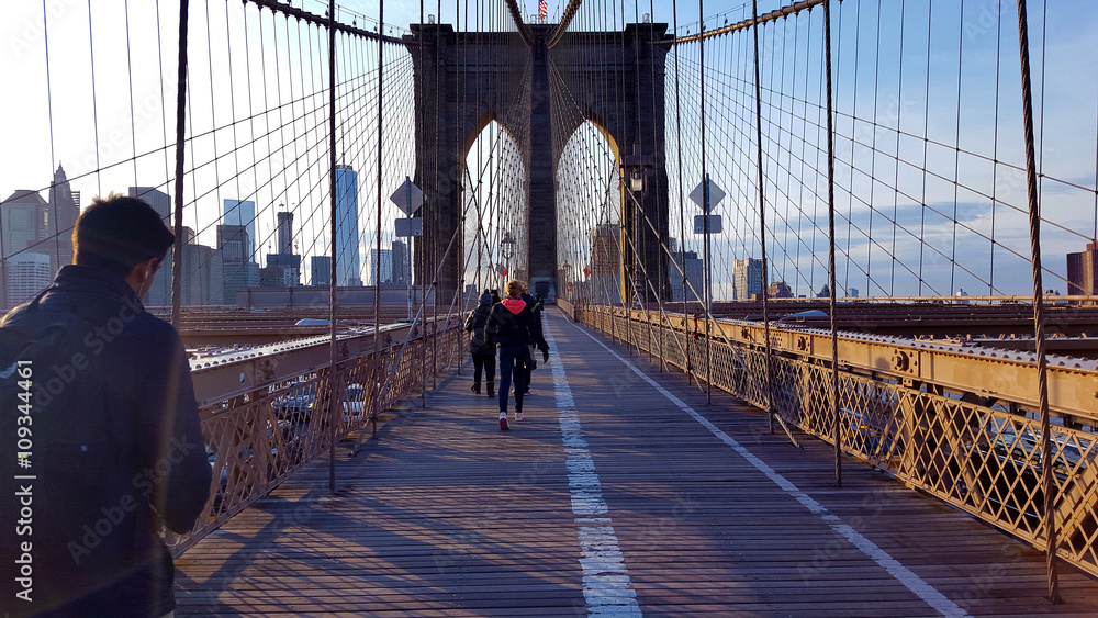 Naklejka premium Ludzie chodzą na Brooklyn Bridge w kierunku Manhattanu wieczorem, Nowy Jork.
