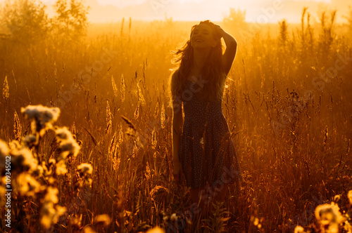 Smiling beautiful girl in fog correct her hair, field, sun backlight, sunrise, orange colors