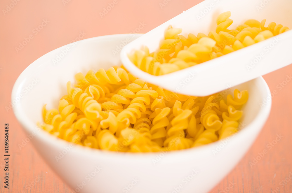 Large kitchen spoon grabbing dry fusilli out from white bowl, professional setting Large kitchen spoon grabbing dry fusilli out from white bowl, professional setting