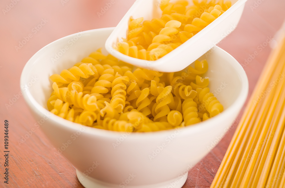 Large kitchen spoon grabbing dry fusilli out from white bowl, professional setting Large kitchen spoon grabbing dry fusilli out from white bowl, professional setting