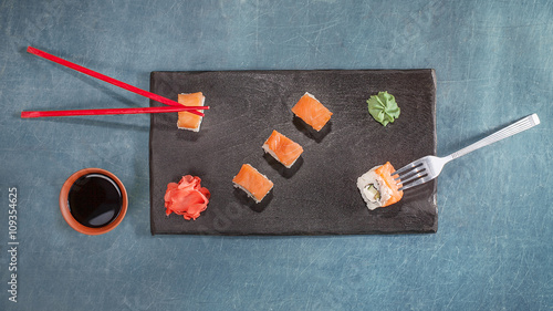 Chopsticks and fork with sushi on black plate
