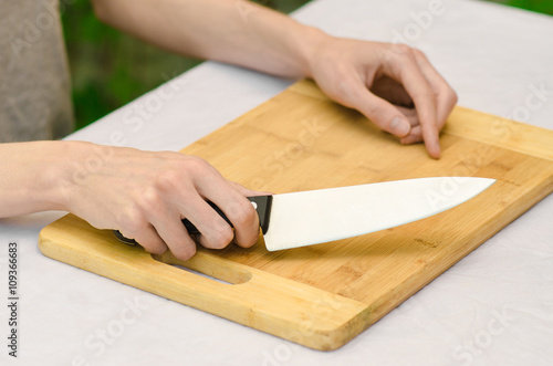 cooking theme: a man holding a knife next to a wooden cutting board on a background of green grass in summer