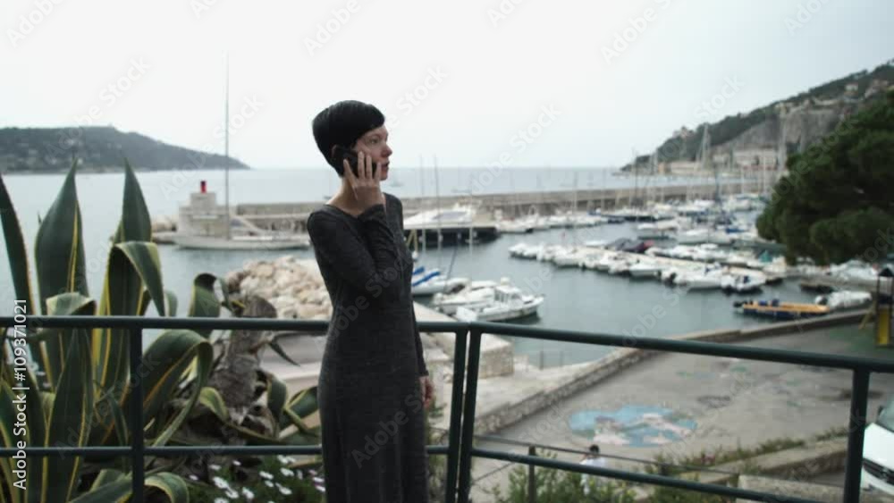 Female standing on the observation deck. On the background marina with yacht and boats and view on the mediterranean city. She looking at the sea. Caucasian model with short haircut dressed grey Female standing on the observation deck. On the background marina with yacht and boats and view on the mediterranean city. She looking at the sea. Caucasian model with short haircut dressed grey