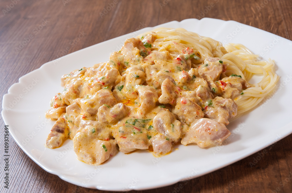 Sliced fried chicken meat in a creamy sauce with spaghetti pasta in a plate on wooden table