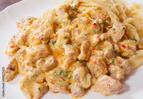 Sliced fried chicken meat in a creamy sauce with spaghetti pasta in a plate on wooden table