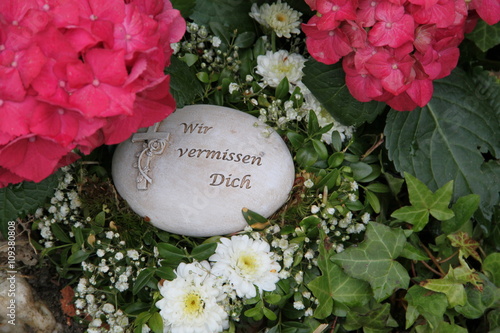 Wir vermissen Dich - Gedenkstein mit Inschrift auf einem Grab zwischen Blumen  photo
