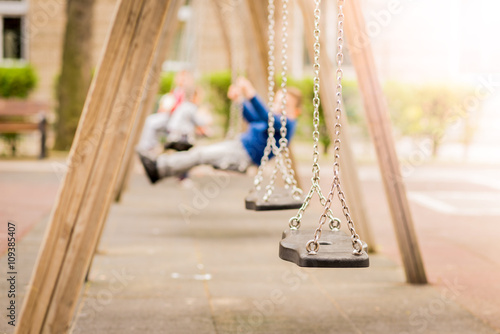 Empty chain swings in a playground. Blured background of swinging kids.