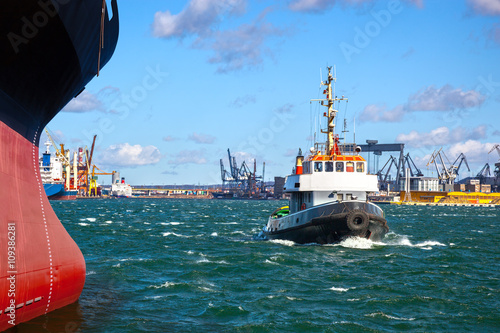 A cargo ship with the assistance of a tugboat in port.