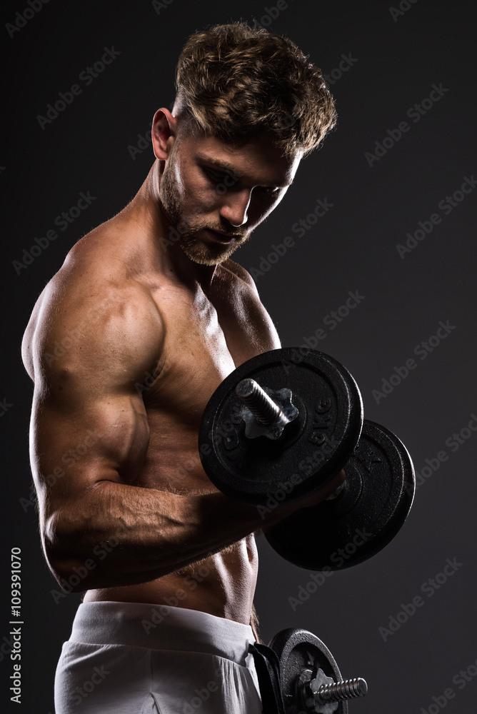 Handsome young bodybuilder training withdumbbells, on grey