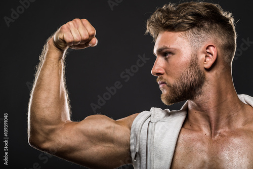 Portrait of handsome young bodybuilder flexing bicep, on grey