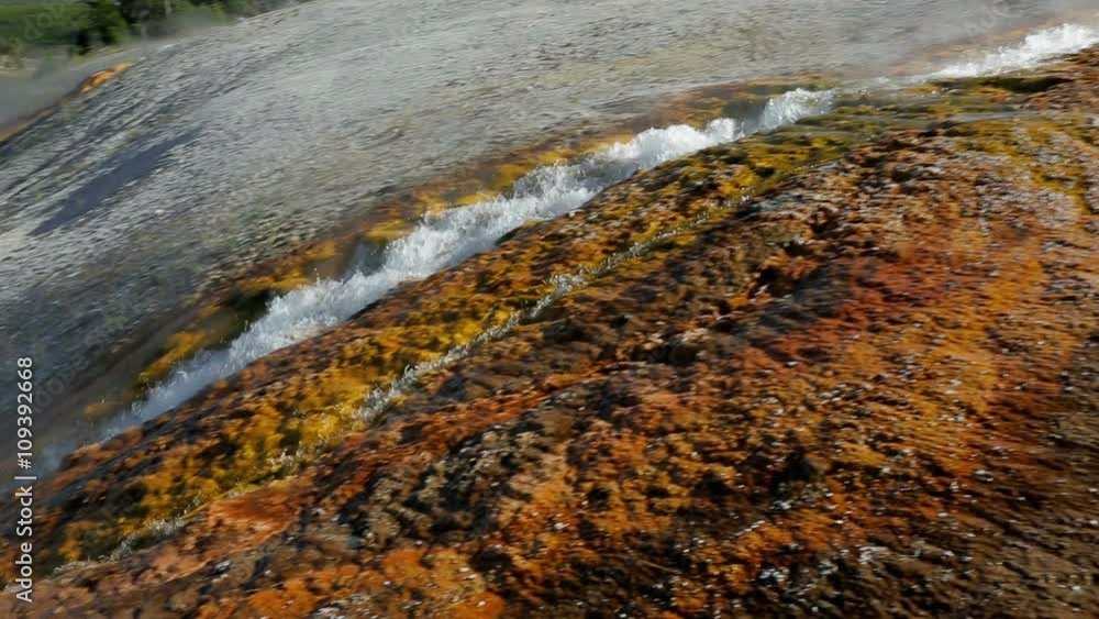 Steaming water streams from a geyser basin and over the rust colored banks of Firehole River in Yellowstone National Park.