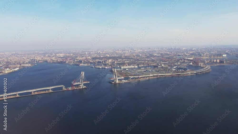 Aerial view from helicopter fly above river. Height. Megapolis at coast. Bridge under construction. Sunny day. Transportation. Aerial view from helicopter fly above river. Height. Megapolis at coast. Bridge under construction. Sunny day. Transportation.