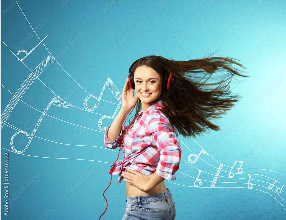 Young woman listening to music and dancing against blue background