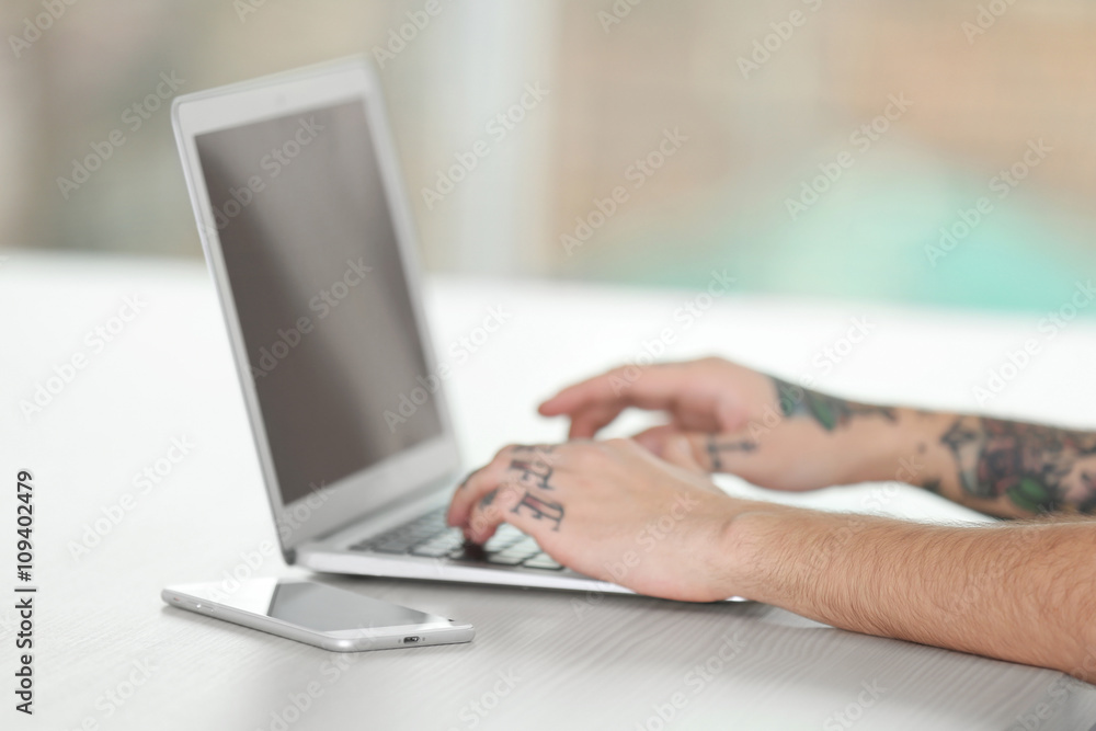 Young man with tattoo using laptop at the table Young man with tattoo using laptop at the table