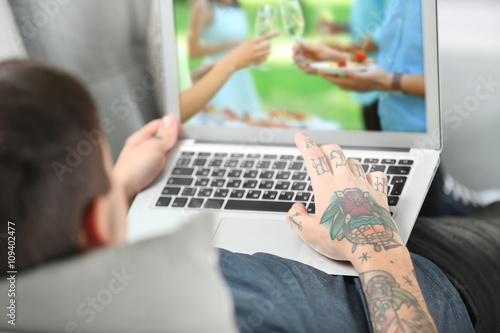 Young man with tattoo using laptop on a sofa at home