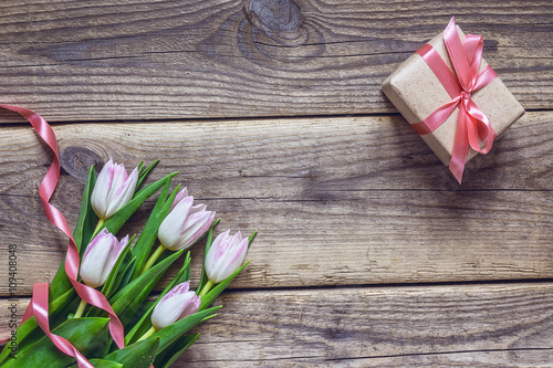 Pink tulips and gift box with rosy ribbon on a  grunge wooden ba