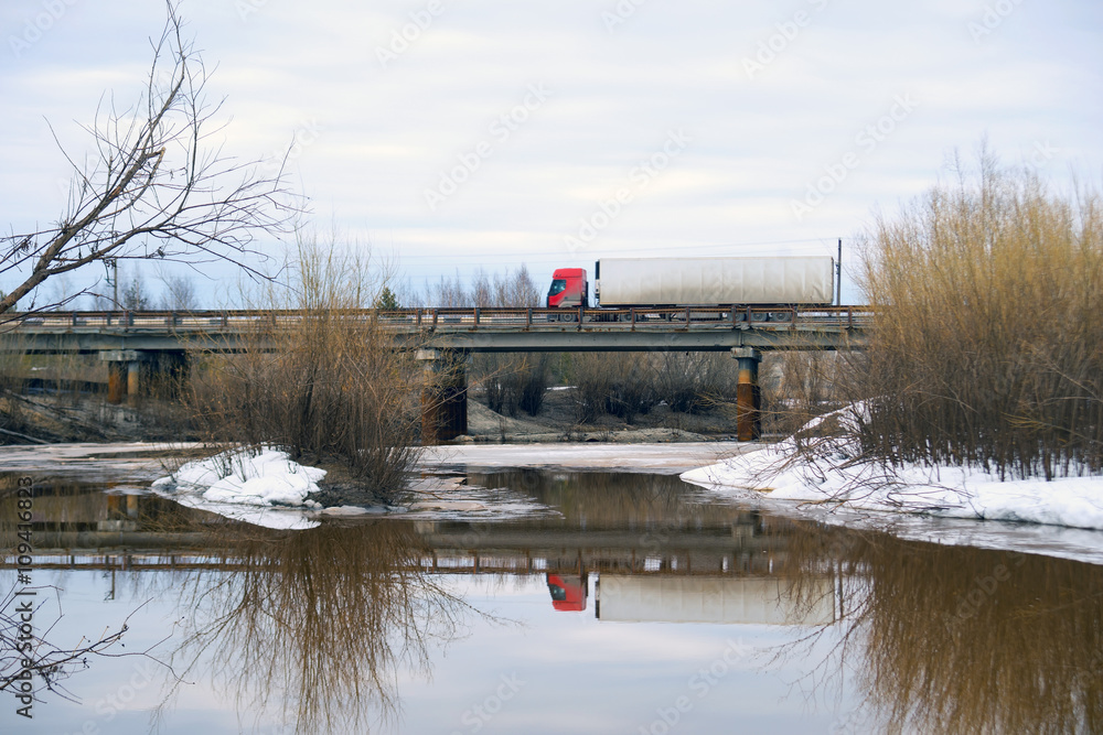 Fototapeta premium Truck driving on a bridge over river in the spring.