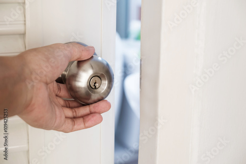 Close-up hand holding door knob, opening door slightly, selective focus