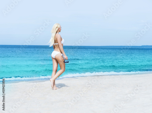 Young blond woman in a white swimsuit on the beach