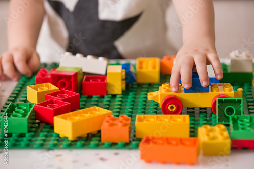 Close up of child's hands playing with colorful plastic bricks at the table. Toddler having fun and building out of bright constructor bricks. Early learning. stripe background. Developing toys