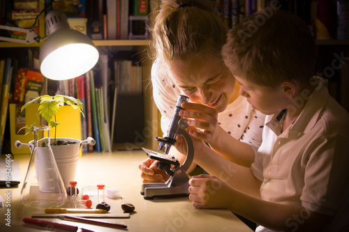 Young mother and elementary school kid boy looking into microscope at home. Family studying samples under the microscope. Science activities with children. Preparing for science lesson. photo