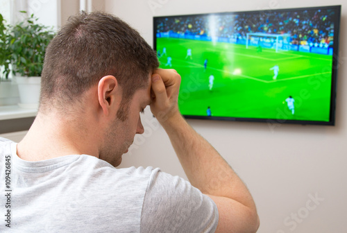 Sad man watching football match on television at home.