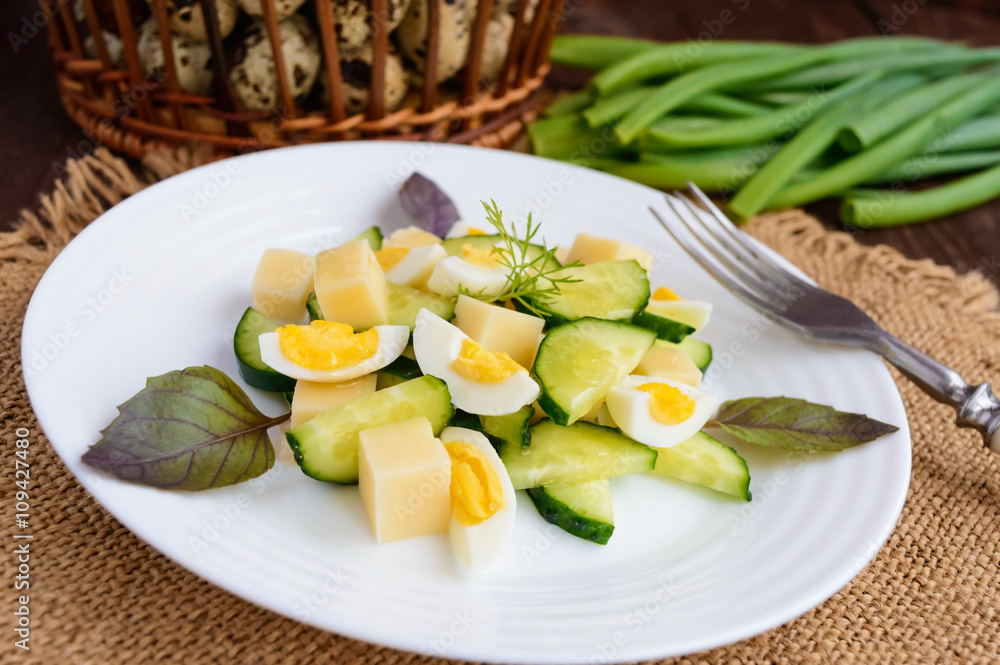 Light Italian Spring salad with fresh cucumber, quail eggs, mozzarella, olive oil on a white plate on a wooden background. Dietary meal.
