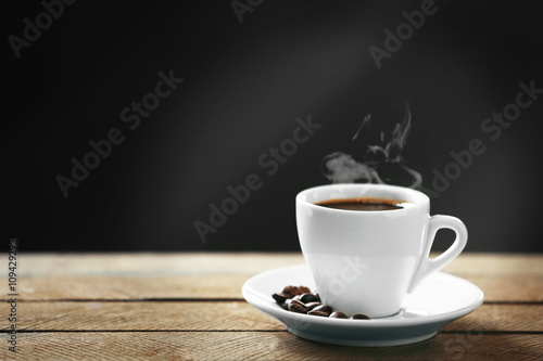 Cup of coffee and coffee grains on wooden table  on gray background