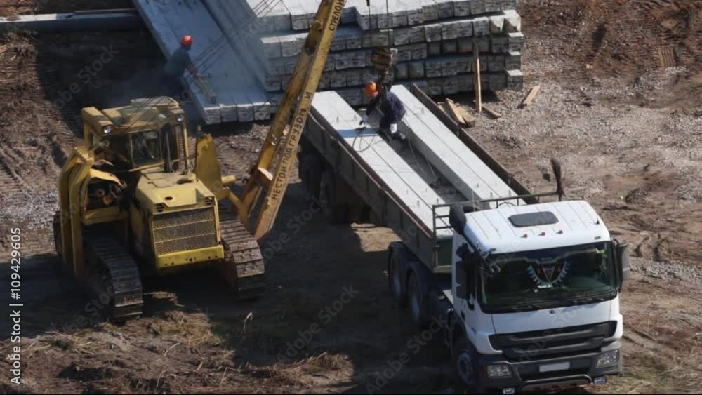 PERM, RUSSIA - SEP 28, 2015: Tractor with crane hook unloads concrete piles on construction site of largest developer Perm factory of silicate panels PERM, RUSSIA - SEP 28, 2015: Tractor with crane hook unloads concrete piles on construction site of largest developer Perm factory of silicate panels
