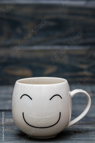 White Cup with Smiley Face on Blue Wooden Table © OZMedia