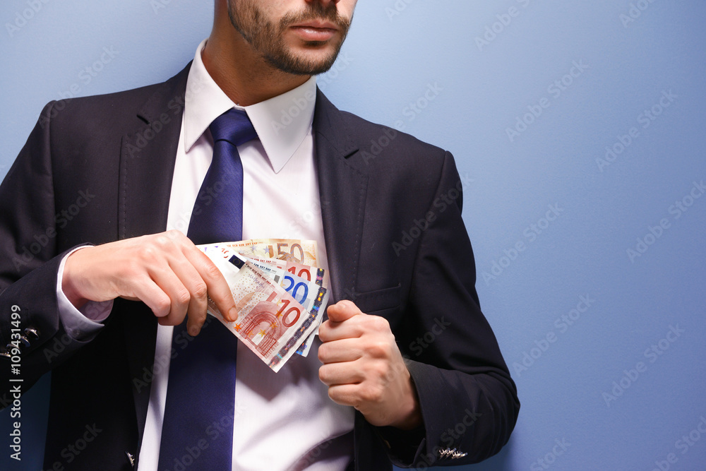 Attractive man hiding euro banknotes in suit on blue background