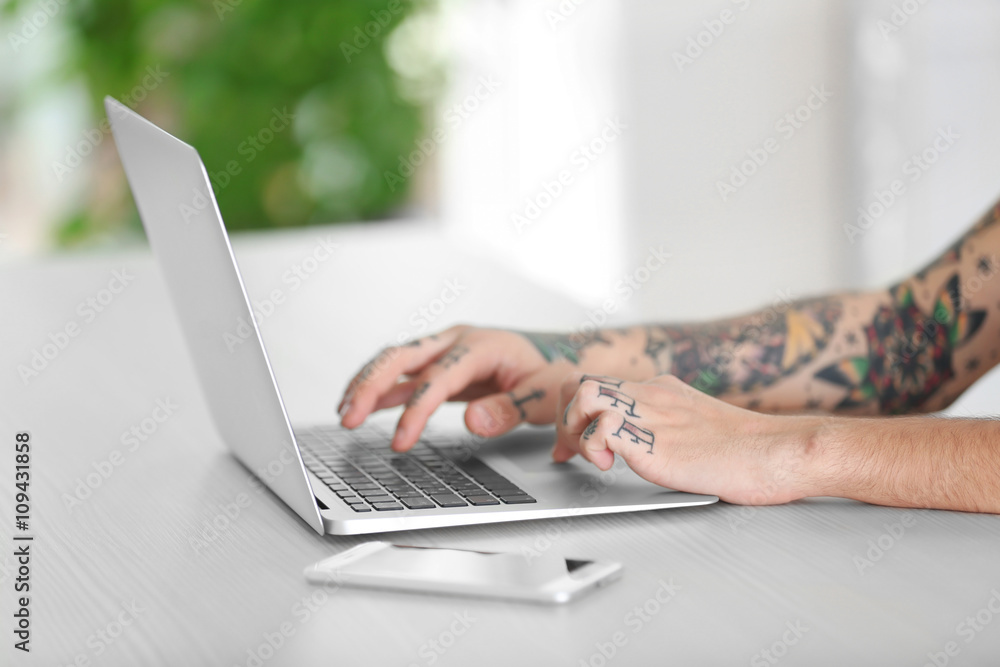 Young man with tattoo using laptop at the table Young man with tattoo using laptop at the table
